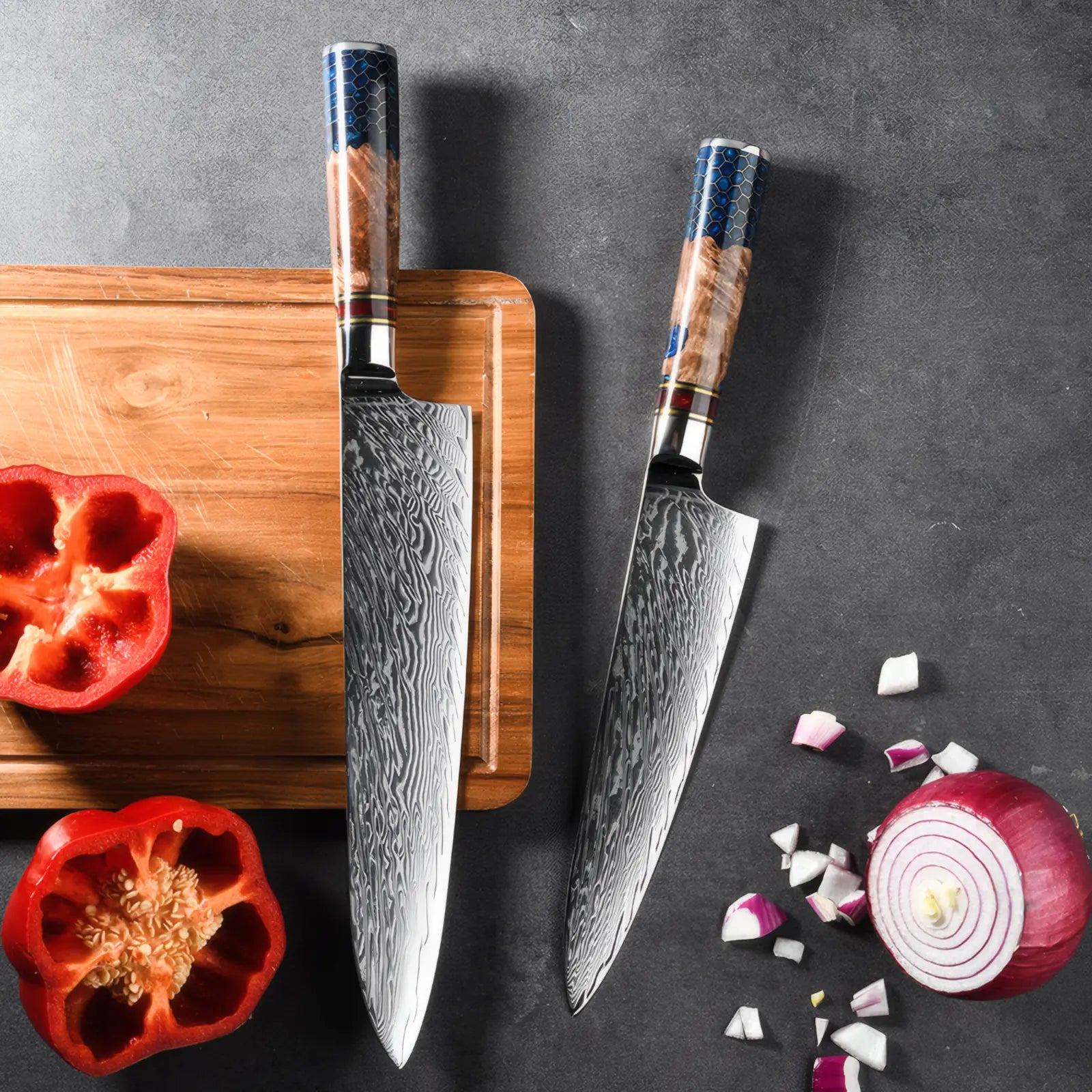 Two chef's knives with wooden handles on a dark surface with cutting board and vegetables.