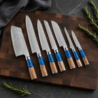 Seven-piece blue resin and wood handle Damascus knife set on a dark walnut board